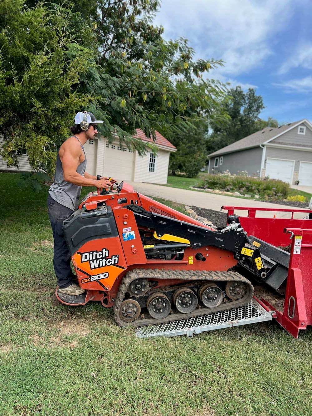 Ditch Witch SK800 skid steer loader on grass with operator loading soil into trailer.