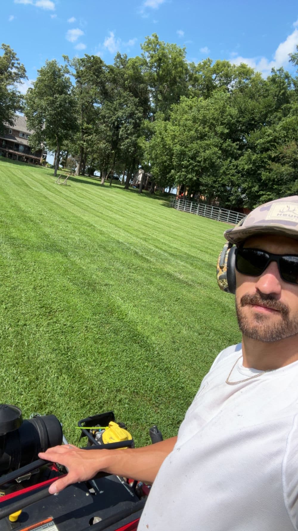 Lawn care professional mowing a perfectly striped lawn in a green, shaded area.