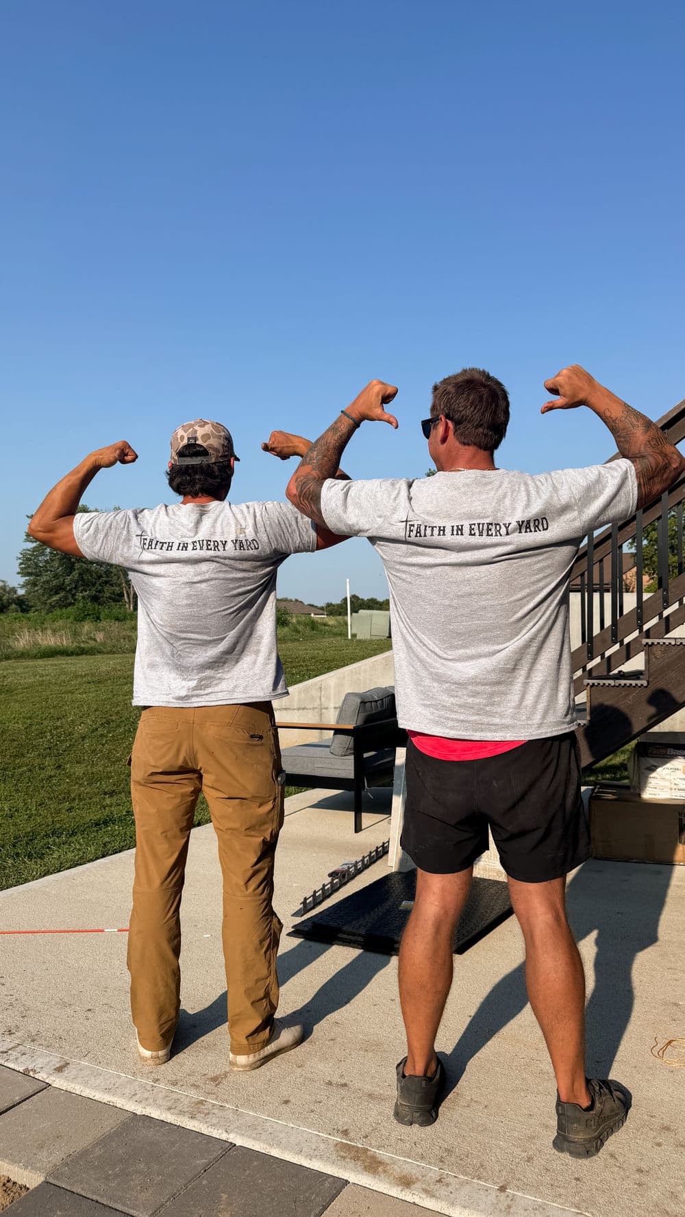 Two men flexing muscles in matching gray shirts that say "Faith in Every Yard."